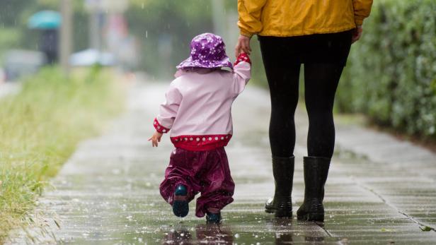 Ein Kind in Regenkleidung geht mit einer erwachsenen Person im Regen spazieren.