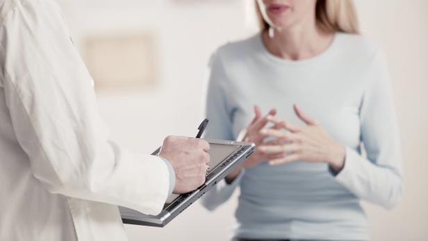 Ein Arzt macht sich Notizen auf einem Tablet, während er mit einer Patientin spricht.