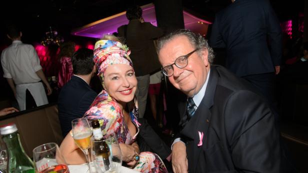 Eine Frau mit Turban und ein Mann im Anzug posieren lächelnd für ein Foto.