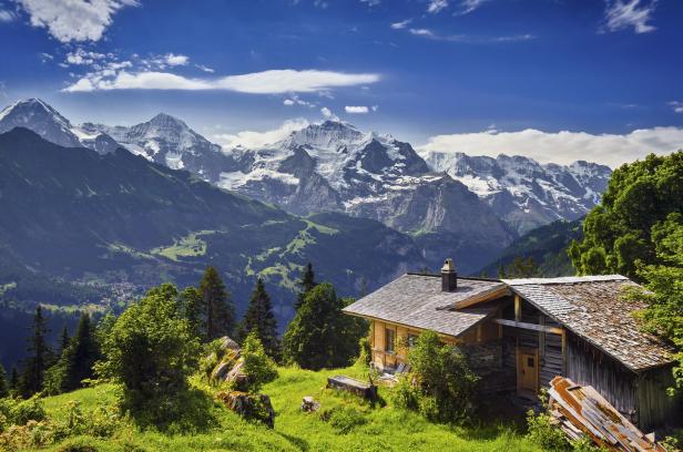Ein Holzhaus vor einer Bergkulisse mit schneebedeckten Gipfeln in den Schweizer Alpen.