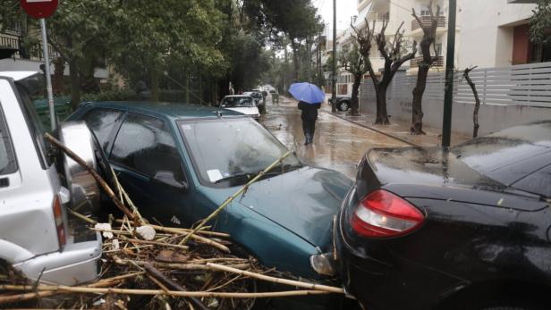 Überschwemmte Straße mit beschädigten Autos und einer Person mit Regenschirm im Hintergrund.
