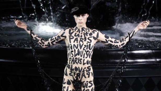 Ein Model mit Körperbemalung mit dem Schriftzug „Paris Louis Vuitton“ auf einer Modenschau.