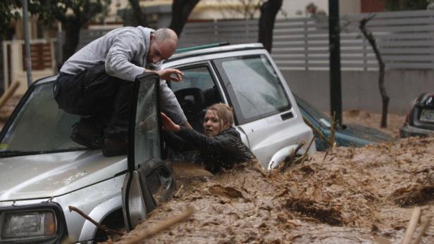 Ein Mann hilft einer Frau, aus einem Auto zu steigen, das in schlammigem Hochwasser steht.