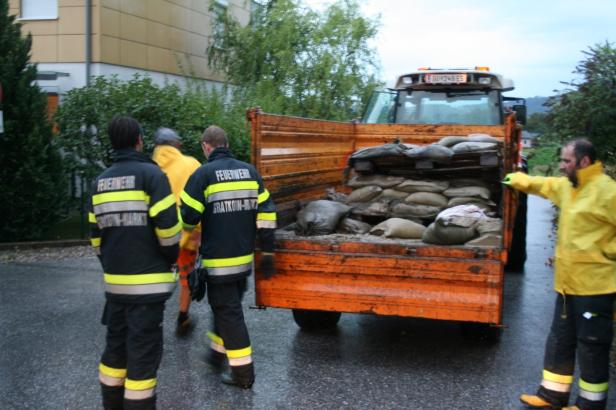 Feuerwehrleute beladen einen Traktoranhänger mit Sandsäcken.