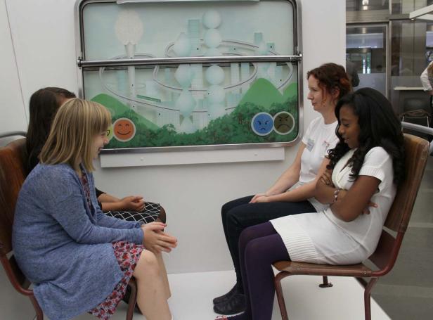 Vier Frauen sitzen vor einer Wand mit einer Grafik, die Emotionen darstellt.