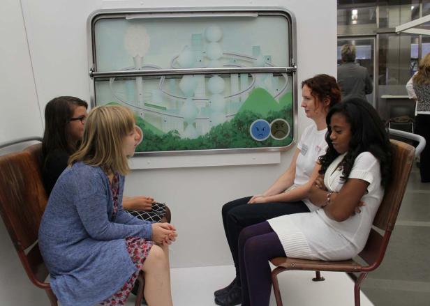 Vier Frauen sitzen in einer Installation, die an eine U-Bahn erinnert.