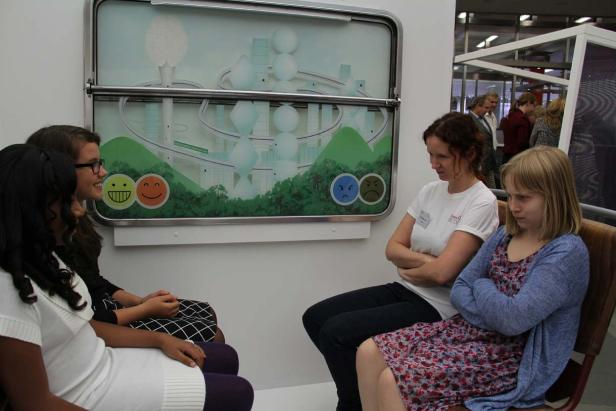 Eine Gruppe von Personen sitzt vor einer Grafik mit stilisierten Stadtansichten und Smileys.