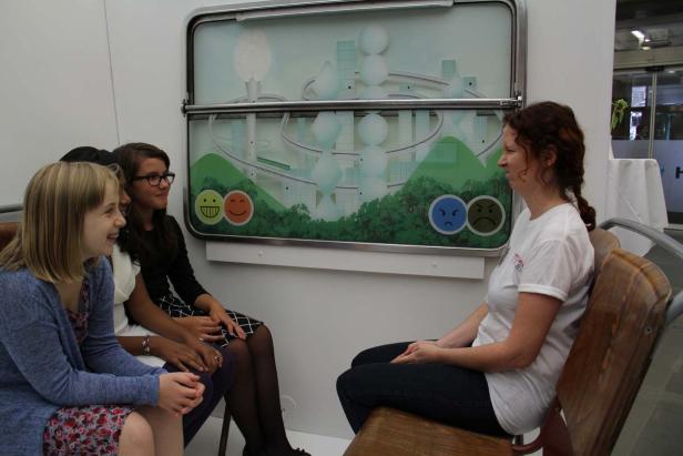 Drei Mädchen und eine Frau sitzen vor einer interaktiven Installation mit Smileys.