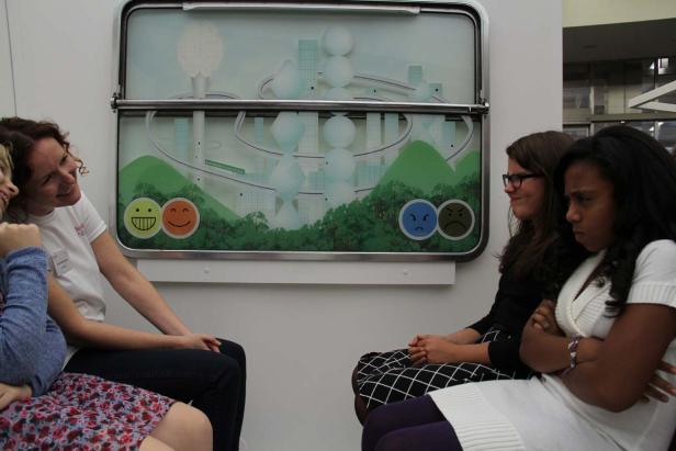 Zwei Frauen sitzen lächelnd neben einem Bild, während zwei andere Frauen daneben unzufrieden wirken.