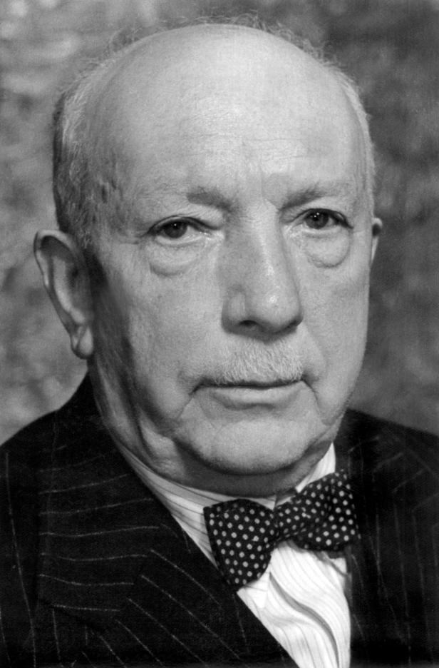 Ein älterer Mann mit Schnurrbart und Fliege in einem gestreiften Anzug.