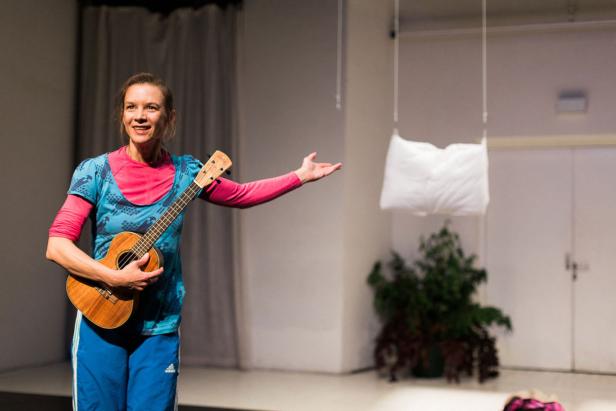 Eine Frau mit Ukulele steht auf einer Bühne und gestikuliert.
