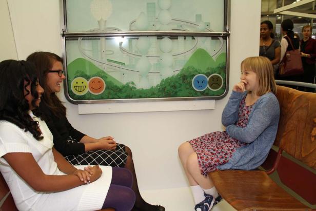 Drei junge Mädchen sitzen vor einer interaktiven Installation mit Smileys und einer Gehirn-Darstellung.