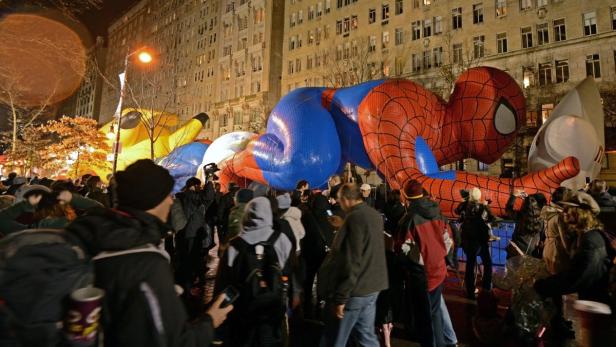 Eine Menschenmenge betrachtet große Ballonfiguren von Spider-Man und anderen Charakteren bei einer Parade.