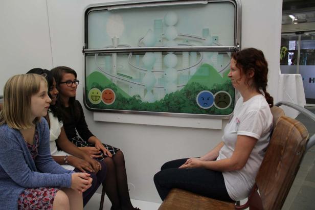 Eine Frau sitzt einer Gruppe junger Mädchen vor einer interaktiven Installation gegenüber.