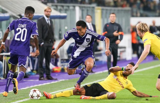 Ein Fußballspieler in Lila überwindet einen am Boden liegenden Spieler in Gelb.
