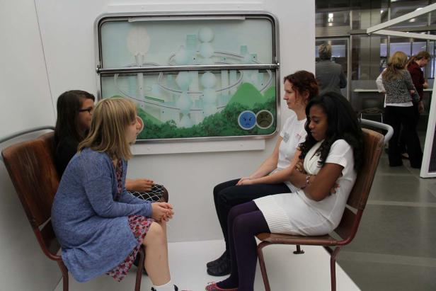 Vier Frauen sitzen in einer Installation, die an einen Zugwagen erinnert.