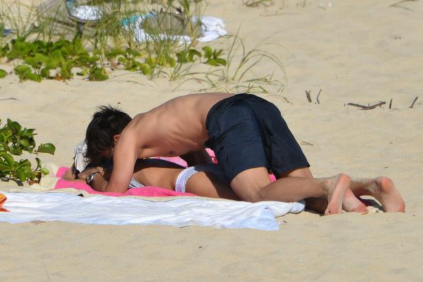 Ein Paar liegt am Strand auf einem Handtuch.