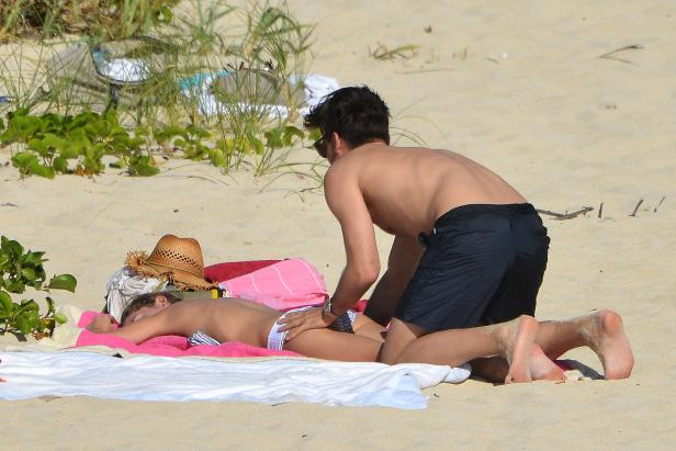 Ein Mann massiert eine Frau am Strand.