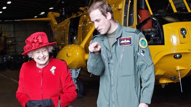 Königin Elisabeth II. und Prinz William vor einem gelben Rettungshubschrauber.