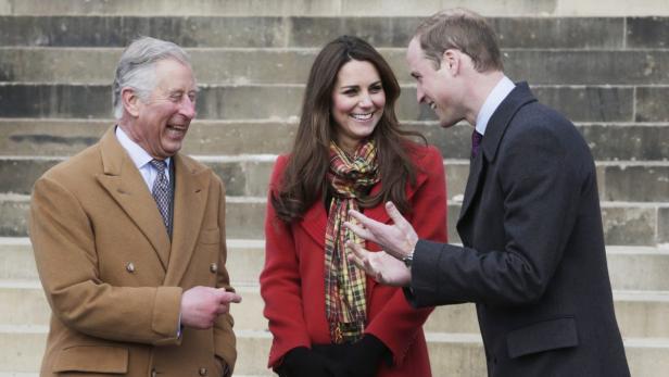 Prinz Charles, Kate Middleton und Prinz William unterhalten sich lachend vor einer Treppe.