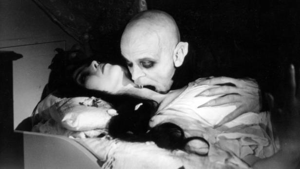 Ein Vampir mit langen Fingernägeln beißt eine schlafende Frau in den Hals.
