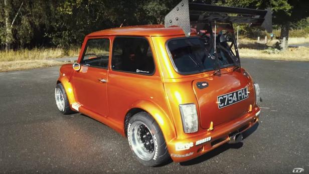 Ein orangefarbener Mini Cooper mit einem großen Heckflügel.