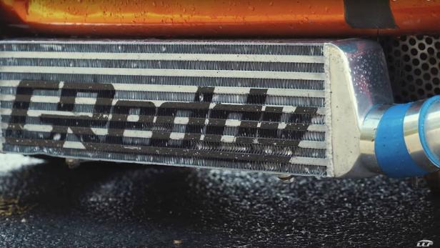 Ein Ladeluftkühler mit dem Schriftzug „Garrett“ ist an einem orangefarbenen Auto montiert.