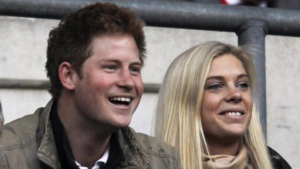 Prinz Harry und eine blonde Frau schauen lächelnd zu.