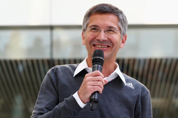 Ein Mann mit Brille lächelt und hält ein Mikrofon.