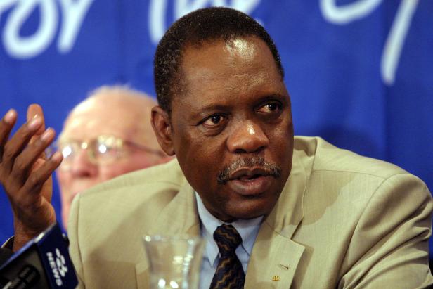 Ein Mann in einem hellen Anzug gestikuliert vor einem blauen Hintergrund.