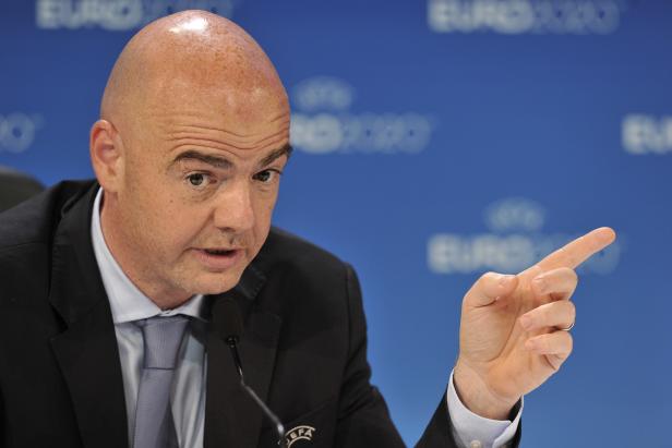 Gianni Infantino gestikuliert bei einer Pressekonferenz vor blauem Hintergrund.