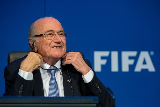 Sepp Blatter lächelt vor einem blauen FIFA-Hintergrund.