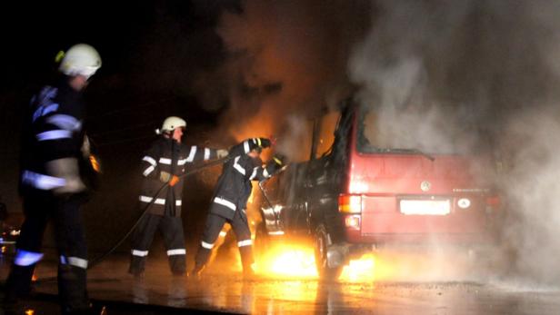 Feuerwehrleute löschen einen brennenden roten VW-Bus.