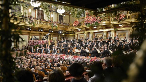 Ein Orchester spielt vor einem Publikum in einem reich verzierten Konzertsaal.