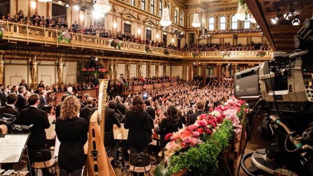 Ein Orchester spielt vor einem großen Publikum in einem opulenten Konzertsaal.