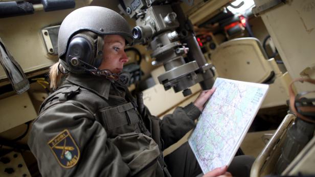 Eine Soldatin mit Helm studiert eine Karte im Inneren eines Panzerfahrzeugs.