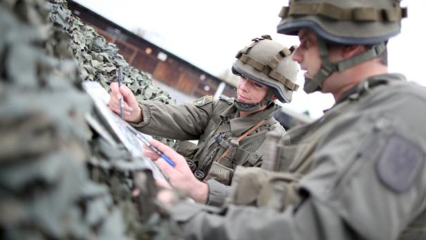 Zwei Soldaten in Uniform und Helm betrachten eine Karte und zeichnen darauf..