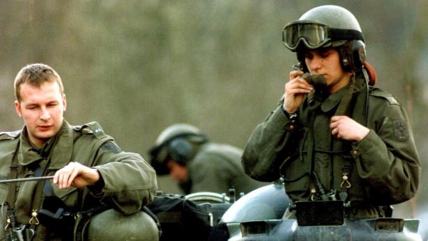 Zwei Soldaten in Uniformen sitzen auf einem Panzer, einer spricht in ein Funkgerät.