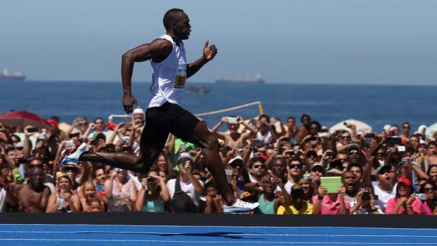Usain Bolt läuft vor einer jubelnden Menschenmenge am Strand entlang.