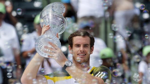 Andy Murray hält eine Trophäe in die Höhe, umgeben von Seifenblasen.