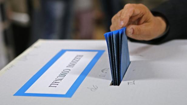 Eine Hand wirft einen blauen Stimmzettel in eine Wahlurne für die Kommunalwahlen.