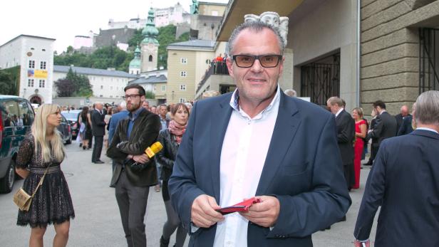 Ein Mann im Anzug steht vor einer Menschenmenge in Salzburg.