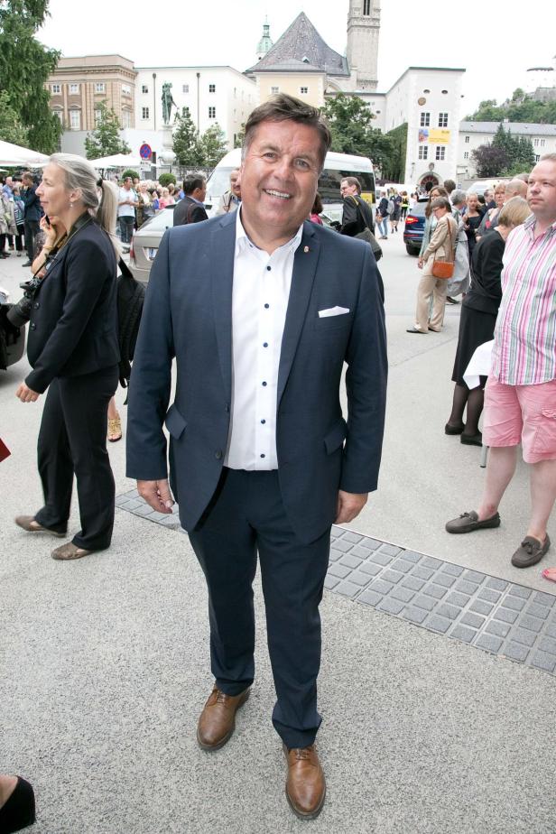 Ein Mann in Anzug steht vor einer Menschenmenge in Salzburg.