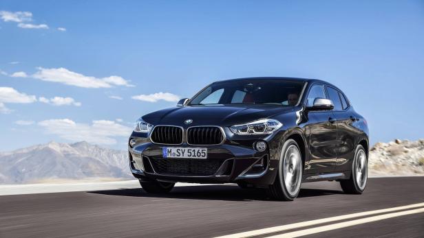 Ein schwarzer BMW X2 fährt auf einer asphaltierten Straße vor einer Bergkulisse.