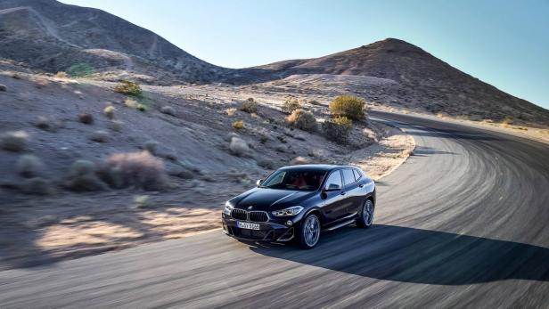 Ein schwarzer BMW X2 fährt auf einer kurvenreichen Straße durch eine Wüstenlandschaft.