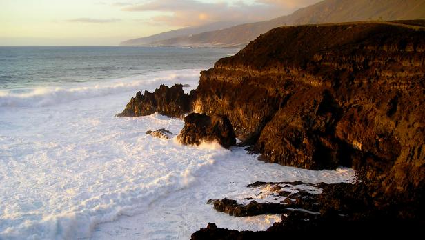 Brandungswellen treffen auf eine felsige Küste im goldenen Licht.
