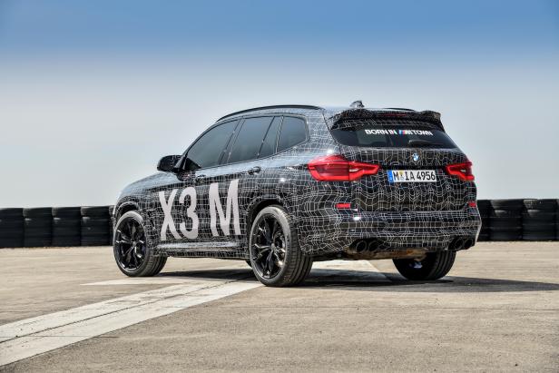 Ein BMW X3 M mit auffälliger Tarnung steht auf einer asphaltierten Fläche.