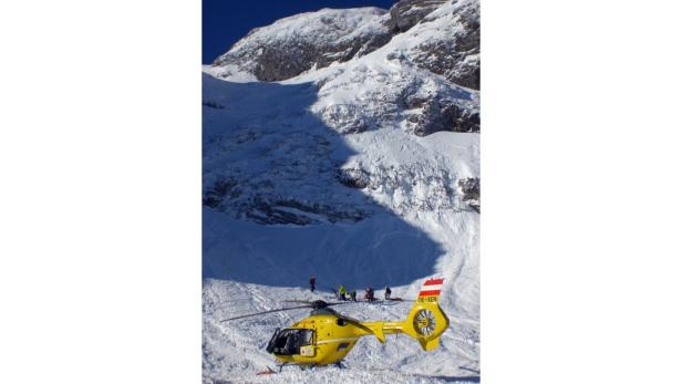Ein gelber Rettungshubschrauber steht vor einer verschneiten Berglandschaft.
