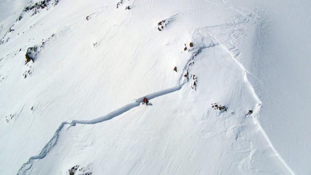 Ein Skifahrer fährt eine steile, schneebedeckte Rinne hinunter.