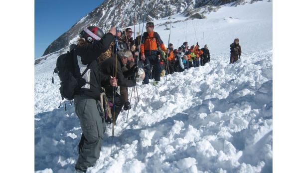 Eine Gruppe Skifahrer steht auf einem schneebedeckten Hang vor einem Berg.